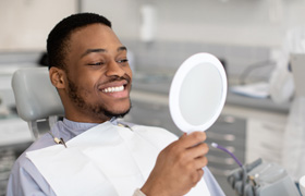 Man checking teeth in mirror after smile makeover in Milton