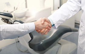 Shaking hands in front of a dental chair