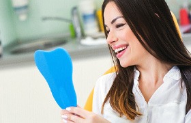 A young woman admiring her new dental crown in a hand mirror